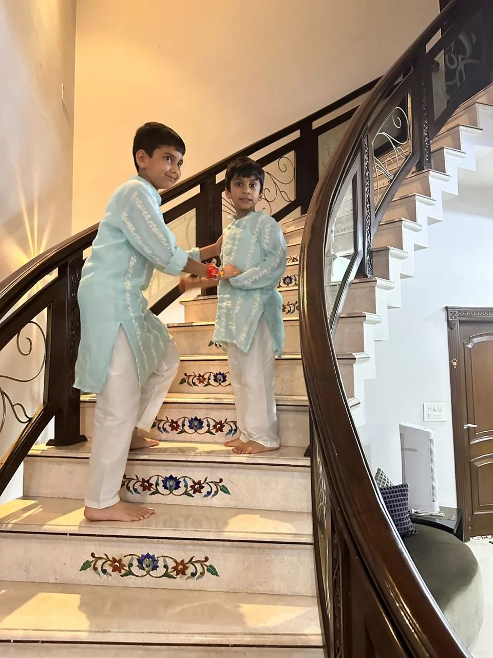 Two boys in pastel kurta sets standing on a staircase