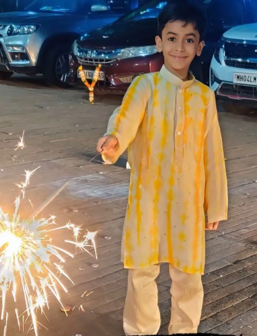 Boy in a yellow tie-dye kurta set holding a sparkler
