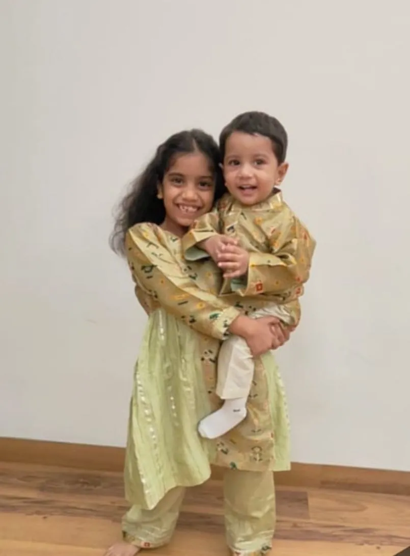 Girl in a pastel sharara set carrying her little brother in a matching outfit