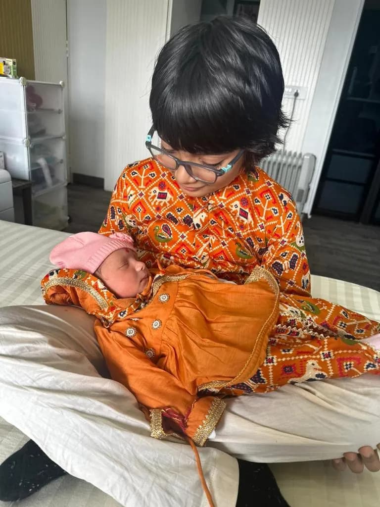 Child in an orange printed kurta holding a newborn